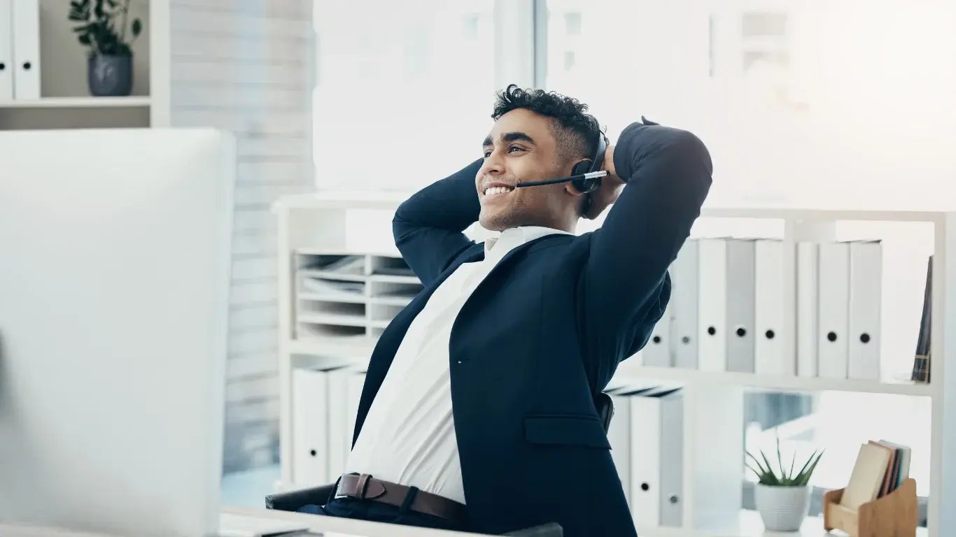 Asesor inmobiliario sonriente y relajado frente a su computadora, logrando una buena gestión de clientes sin desorden.